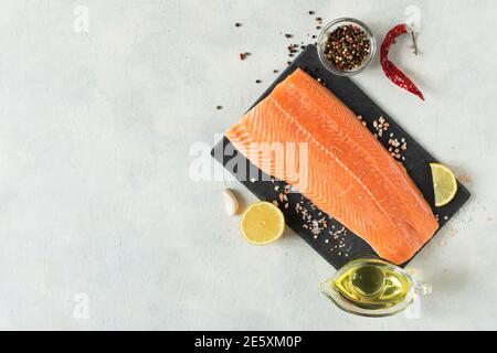 Frisches rohes Lachsfischfilet mit Kochgewürzen, Öl und Zitrone auf schwarzem Schieferbrett über grauem Beton-Hintergrund Draufsicht. Gesunde Ernährung voller om Stockfoto