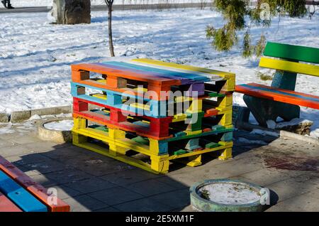 Modernes Street Art Konzept. Ein Sitzbereich auf einer Stadtstraße aus bunten Paletten. Bunte Bänke und Tisch. Sonniger Wintertag. Keine Personen. Stockfoto