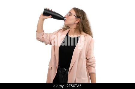 Eine Frau in einem Anzug trinkt aus einer wiederverwendbaren Wasserflasche. Die Geschäftsfrau trägt eine Brille. Isoliert auf weißem Hintergrund. Stockfoto