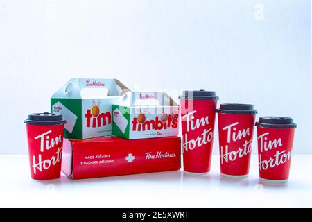 Calgary, Alberta. Kanada. Januar 28 2021. Mehrere Tim Hortons Kaffeetassen in verschiedenen Größen mit Schachteln aus Timbits und Donuts auf weißem Hintergrund. Stockfoto