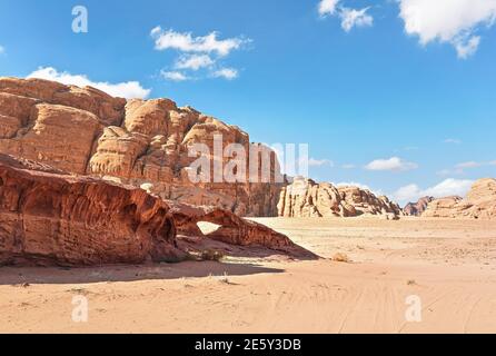 Kleiner Bogen oder kleine Felsenfensterformation in der Wadi Rum Wüste, helle Sonne scheint auf rotem Staub und Felsen, blauer Himmel darüber Stockfoto