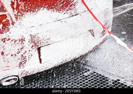 Rotes Auto gewaschen in selbst dienen Autowäsche, Detail auf weißem Seifenschaum Sprühen von Hochdruckschlauch auf hinteren Kennzeichen Stockfoto