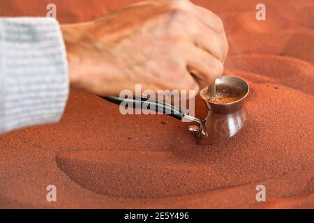 Kaffee, der auf der Straße auf traditionelle arabische Weise zubereitet wird, wird in roten heißen Sand gelegt, bis Flüssigkeit kocht, Detail Stockfoto