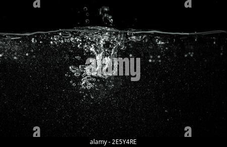 Wasser, das in das Aquarium fließt, schwarzer Hintergrund, Detail auf abgefallene Flüssigkeit, die weiße Blasen und abstrakte Formen erzeugt