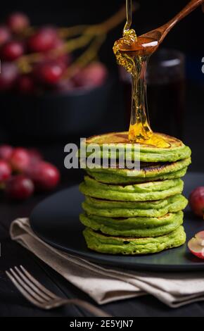 Grüne Pfannkuchen mit Matcha-Tee oder Spinat, gekleideten Honig und roten Trauben. Ideen und Rezepte für ein gesundes Frühstück mit Superfood-Zutaten. Dunkler Rücken Stockfoto