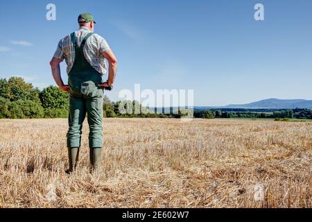 Nach der Ernte steht ein Bauer auf seinem gemähten Getreidefeld und genießt den Blick über das weite Land bis zu den Ausläufern der Schwäbischen Alb Stockfoto