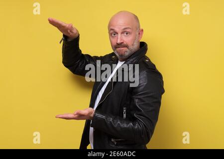 Reifer bärtiger Mann prahlte über die große Größe von etwas. Studio auf gelber Wand. Stockfoto