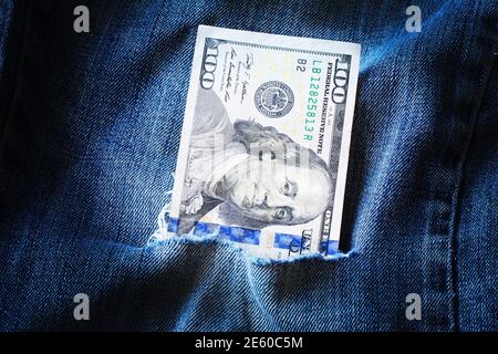 Hundert Dollar in zerrissenen blauen Jeans. Armut und Reichtum in zerrissenen Kleidern. Diebstahl von Haushaltsmitteln, Korruption, Diebstahl Stockfoto