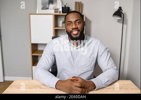 Ein junger und energiegeladener afroamerikanischer Freiberufler ist bereit für ein Online-Interview bei einem Videoanruf, sitzt am Schreibtisch und schaut auf die Kamera Stockfoto