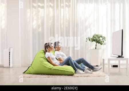 Junger Mann und Frau sitzen auf grünen Bohnenbeutelsesseln Und Fernsehen zu Hause Stockfoto