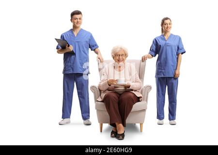 Eine Krankenschwester und eine Krankenschwester stehen neben einer älteren Frau Sitzen in einem Sessel isoliert auf weißem Hintergrund Stockfoto