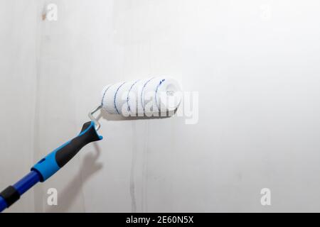 Männliche Hand mit einer Rolle zum Malen von Wänden. Der Maler trägt dekorative Farbe auf die Wand.Reparatur im Inneren des Hauses.Roller Wandmalerei. Arbeiter Stockfoto