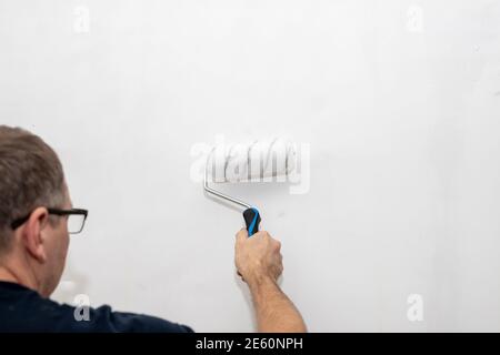 Männliche Hand mit einer Rolle zum Malen von Wänden. Der Maler trägt dekorative Farbe auf die Wand.Reparatur im Inneren des Hauses.Roller Wandmalerei. Arbeiter Stockfoto