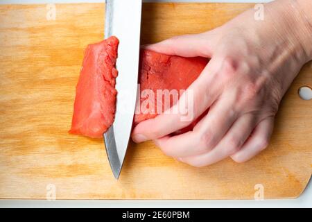 Frau schneidet ein Stück roten Fisch mit einem Messer auf einem hölzernen Schneidebrett. Sushi kochen, Schritt 1 Stockfoto