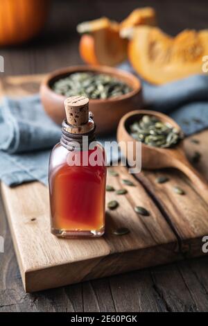 Kaltgepresstes Kürbiskernöl in einer Glasflasche, verziert mit geschälten Samen auf einem Holztisch Stockfoto