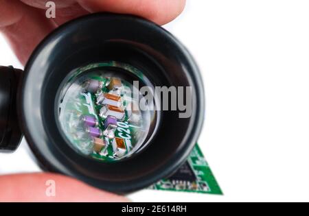 Miniatur-Induktivitäten, Widerstände und Kondensatoren in Lupe auf weißem Hintergrund. Halbleiterelektronik auf grüner Leiterplatte. Technik. Stockfoto