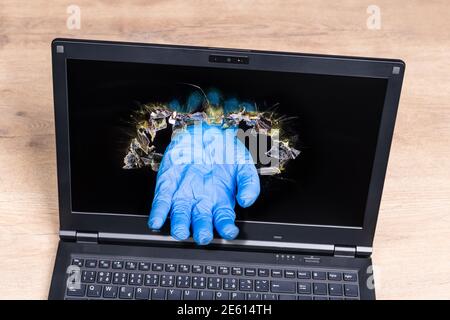 Laptop-Detail mit imaginären helfenden Hand in blauen Handschuh ragt aus dem Lochloch im Display. Entfernung Gesundheitskonzept bei Coronavirus-Krankheit. Stockfoto