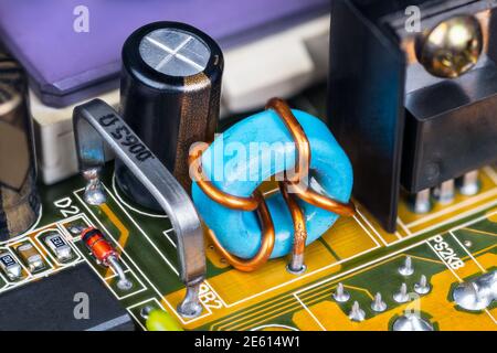 Elektronische Komponenten auf der Leiterplatte innerhalb der Computer-Hardware. Niederohmischer Open-Air-Widerstand, toroidale Induktivität und Kondensator auf Leiterplatte Detail. Stockfoto