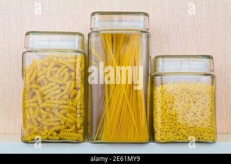 Glasgefäße mit verschieden geformten Nudeln auf weißem Küchenregal Stockfoto