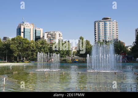 Tirana, Albanien - 21. Juli 2012: Der Brunnen im Rinia Park, dem zentralen öffentlichen Park von Tirana, auf dem Hintergrund einige Wolkenkratzer; der Wolkenkratzer auf dem Stockfoto