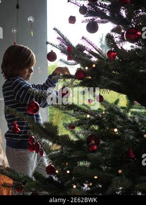 Winterurlaub, Wohltätigkeitsorganisation und Menschen Konzept. Happy boy Dekoration weihnachtsbaum zu Hause. Stockfoto