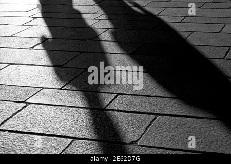 Schatten von Menschen, die bei Sonnenuntergang auf dem Steinboden der vorpandemischen Stadt Mailand, Lombardei, Italien, spazieren gehen Stockfoto