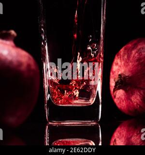 Glas in der dezentralen Beleuchtung mit zwei Granatäpfeln und Saft. Hochwertige Fotos Stockfoto