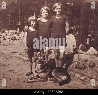 DEUTSCHLAND - 1928: Vintage Foto zeigt 3 junge Mädchen im Sommer. Mädchen tragen Badeanzug und Pose mit Schäferhund. Foto mit Sepia-Effekt. Stockfoto