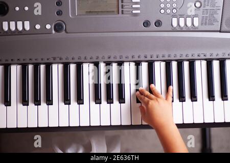 Draufsicht auf die Hand eines Kindes, das Musik auf einem spielt Elektronischer Synthesizer im Wohnzimmer Stockfoto