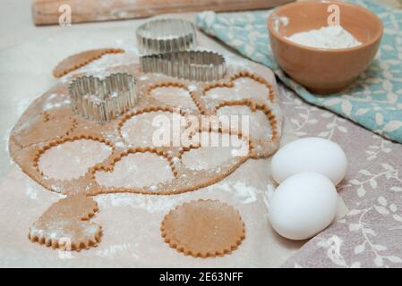 Ausschneiden von herzförmigen Plätzchen aus rohem Teig mit Ausstechformen. Stockfoto