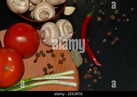 Nahaufnahme von frischen Pilzen, rotem Paprika, Tomaten, Knoblauch, Lorbeerblatt und Piment. Dunkler Hintergrund Stockfoto