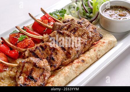 Schweinefleisch, Lammrippen auf Pita-Brot, mit gebackenem Paprika und Sauce, auf einem weißen Teller, auf weißem Hintergrund Stockfoto