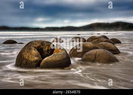 Die berühmten riesigen, runden Felsbrocken am Moeraki-Strand Mit der Flut kommt in einer langen Exposition gefangen Foto Stockfoto