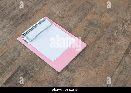 Kleine rosafarbene Klemmbretter mit einem leeren Blatt Papier auf Holzhintergrund Stockfoto