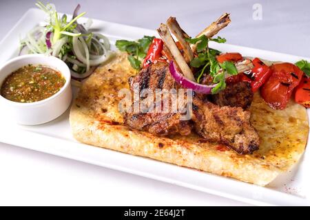 Schweinefleisch, Lammrippen auf Pita-Brot, mit gebackenem Paprika und Sauce, auf einem weißen Teller, auf weißem Hintergrund Stockfoto