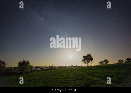 halbmond und Milchstraße über Wiese mit Bäumen außerhalb ein deutsches Dorf in der eifel Stockfoto