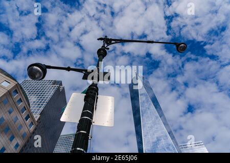 Blick in den Himmel mit einem hohen Laternenpfosten in der Mitte des Rahmens, umgeben von Gebäuden und dem Freedom Tower Stockfoto