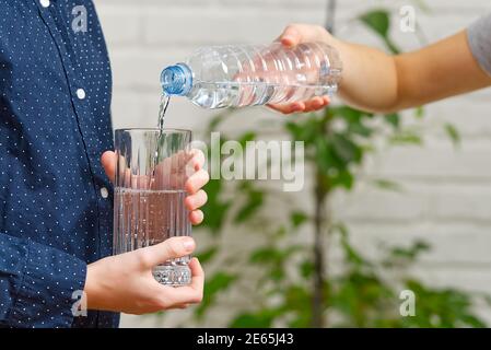 Junge gießt Wasser aus der Plastikflasche in die Glas auf Holztisch Stockfoto