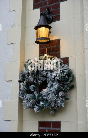 Frostgrüner Weihnachtskranz, der unter einer Laterne auf dem hängt Wand eines Hauses Stockfoto
