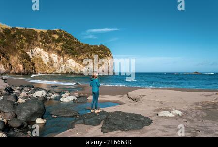 Eine Person am Strand, Frau, Solo, schwarzer Sand, Azoren, Sao Miguel Insel, Reiseziel. Stockfoto