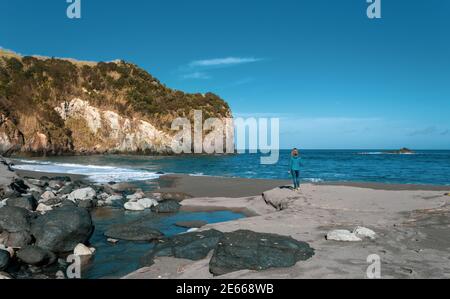 Eine Person am Strand, Frau, Solo, schwarzer Sand, Azoren, Sao Miguel Insel, Reiseziel. Stockfoto
