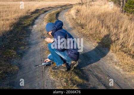 Ein Mann Tourist mit einer Fernbedienung, installiert eine Drohne auf einem Feldweg an einem klaren sonnigen Tag, um Fotos und Videos von der herbstlichen Natur zu machen. Stockfoto