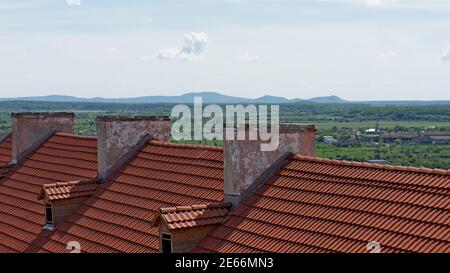 Ziegeldach und alte Kamine Teil des Schlosses Gebäude auf dem Hintergrund des Horizonts, Berge und einsame Wolken Stockfoto