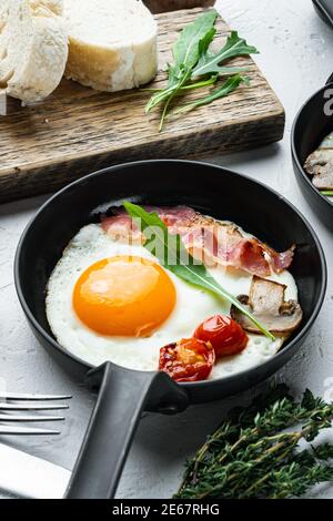 Spiegeleier mit Speck und Gemüse in gusseiserner Bratpfanne, auf weißem Hintergrund Stockfoto