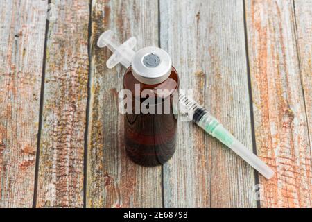 Eine Nahaufnahme einer hygienischen Einweg-Spritze aus Kunststoff mit einem braunen Fläschchen auf einem Holzhintergrund. Stockfoto