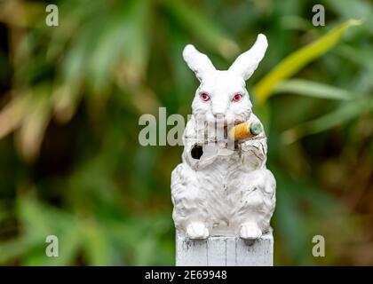 Damage weißes Porzellan Kaninchen Skulptur mit Karotte in grünem Hintergrund Stockfoto