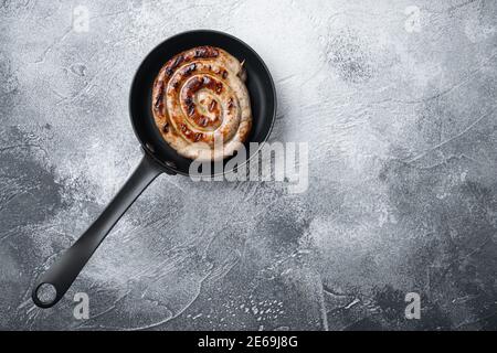 Gegrillte Spiralwurst in gusseiserner Bratpfanne, auf grauem Hintergrund, Draufsicht flach liegend, mit Platz für Text-Copyspace Stockfoto