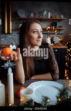 Eine schöne junge Frau in einem schwarzen Kleid sitzt am Tisch und hält ein Lebensmittelgeschäft. Stockfoto