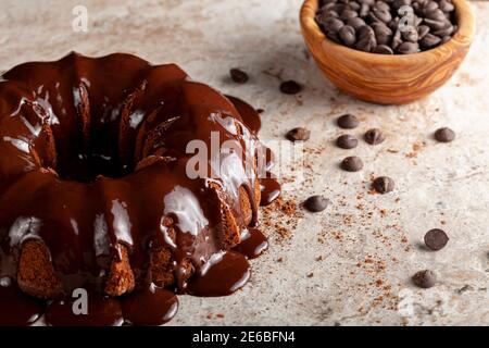Abgewinkelte Ansicht eines Schokoladen-Bunt-Kuchens mit Schokoladenpudding-Glasur, die darauf tropft. Es gibt Kakaopulver und Schokoladenchips auf der Oberfläche wi Stockfoto