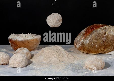 Ein gerundeter Brotteig fällt auf einen Mehlhaufen auf der Marmorplatte. Auf dem Boden gibt es Brote und Teige eine Schüssel mit Mehl und ein ru Stockfoto